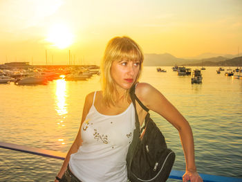 Portrait of beautiful woman standing at harbor against sky during sunset