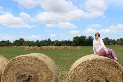 Woman on hay bales on field against sky