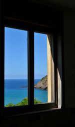Sea against clear blue sky seen through window
