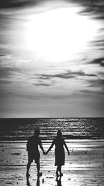 Silhouette friends on beach against sky