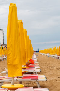 Row of multi colored chairs on beach against sky