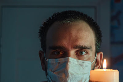 The face of a man wearing a medical mask with a burning candle. close-up person