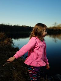 Girl standing by pink lake against clear sky