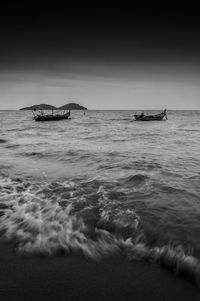 Mid distance view of fishing boats moored in sea against sky