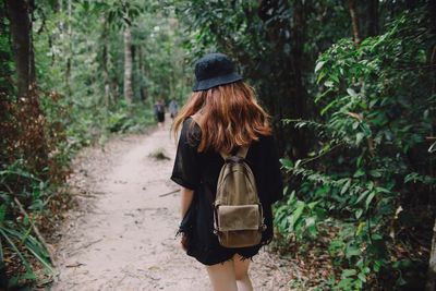 Rear view of backpack woman walking on footpath in forest