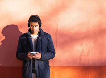 Young man using mobile phone against wall