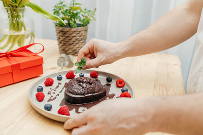 Close-up of a man's hands decorating a chocolate heart cake with a sprig of fresh mint 