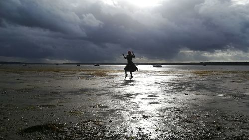 Woman dancing at beach against cloudy sky