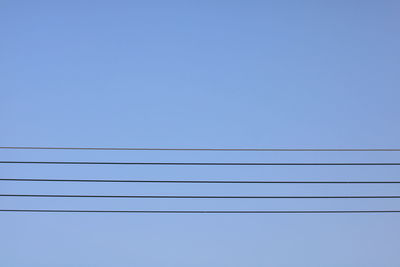 Low angle view of power lines against clear blue sky