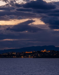 Illuminated city by sea against sky during sunset