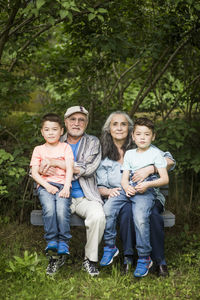 Portrait of grandparents sitting with twin grandsons on bench against plants in back yard