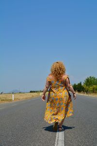 Rear view of woman on road against clear blue sky