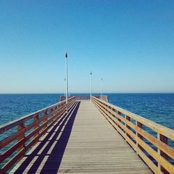 Pier on sea against clear blue sky