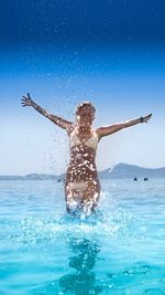 Woman with arms outstretched wearing bikini while running in sea against sky