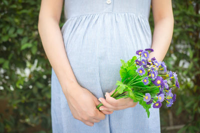 Midsection of pregnant woman holding artificial purple flowers at park