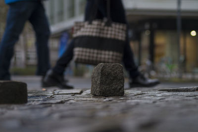 Close-up of rock on street while people walking in background