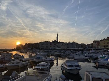 Sailboats moored in harbor against sky during sunset