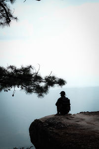 Rear view of silhouette man sitting on rock against sky