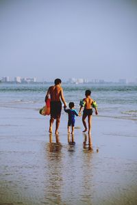 Rear view of family walking on beach against clear sky