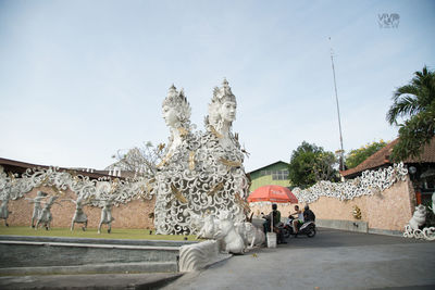 People walking by statue against sky