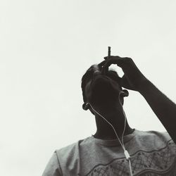 Low angle view of man smoking cigarette while listening to music against clear sky