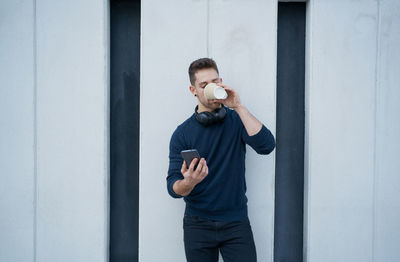 Side view of a modern man in casual clothes sitting near a white wall