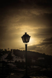 Silhouette street light by building against sky at sunset