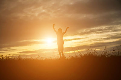 Silhouette woman standing on field against sky during sunset