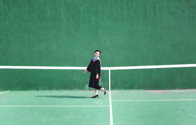 Full length portrait of young woman standing at tennis court