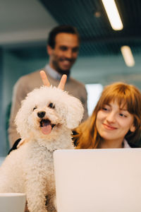 Low angle view of dog with smiling businesswoman against businessman standing at creative office