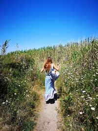Woman walking on field against clear blue sky
