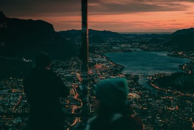 Silhouette man looking at illuminated cityscape against sky during sunset