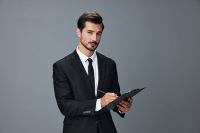 Young man using digital tablet while standing against gray background