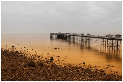 Scenic view of sea against grey sky with pier and morning sand