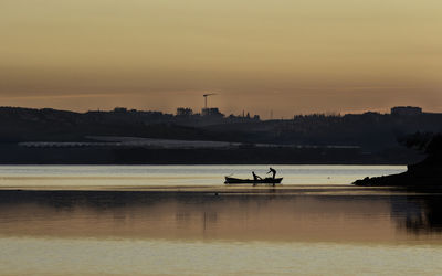 Silhouette boat sailing on river against sky during sunset