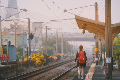 Rear view of woman walking on railroad tracks against sky