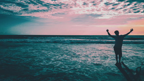 Man with arms outstretched standing in sea against sky during sunset