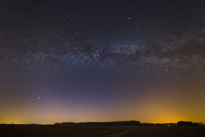 Milky way over the field, with city lights over the horizon.