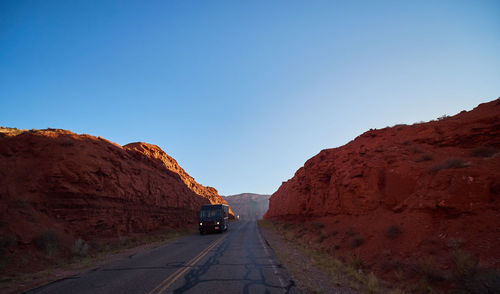 Road amidst rocky mountains against clear blue sky
