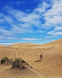 Shirtless man walking on sand in desert against sky