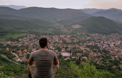 Rear view of man looking at town while sitting on mountain