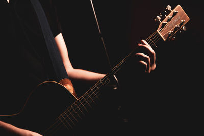 Midsection of person playing guitar against black background