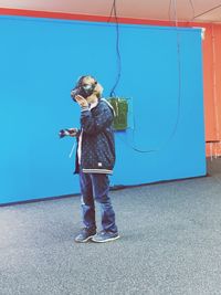 Full length of girl wearing virtual reality headset against blue wall