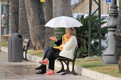 Couple sitting with umbrella on bench during rainy season