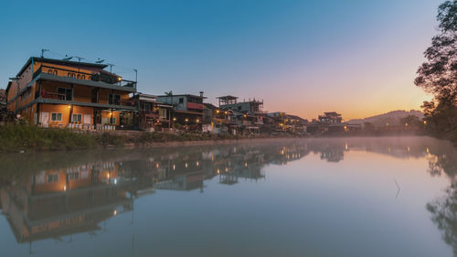 Lake and buildings against sky during sunset