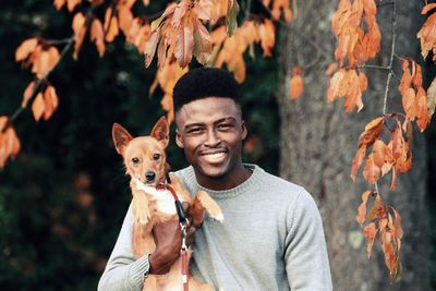 Portrait of smiling man with dog against autumn leaves