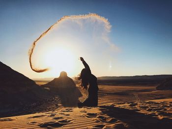 Woman throwing sand at desert against sky