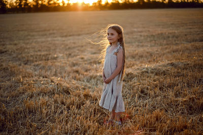 Girl child with long hair walking across the field wearing with long hair during sunset