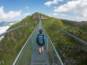 Rear view of woman on footbridge against sky