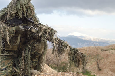 Army man in ghillie suit with rifle on field